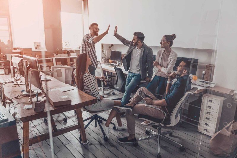 Buyers agents having a casual team meeting with two members celebrating an auction win by giving a high five